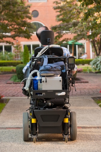 Rear view of a man with Duchenne muscular dystrophy in a motorized wheelchair on the street